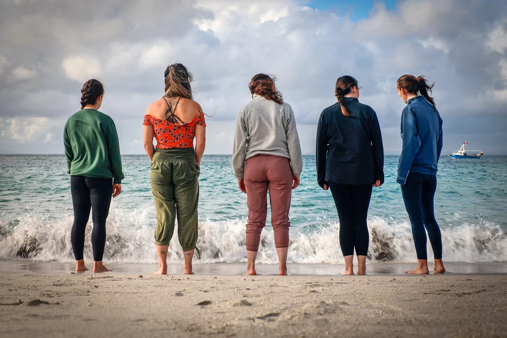 Group of five women standing barefoot on a beach, gazing at the ocean waves, embodying the tranquil spirit of Éalú Aran’s wellness retreats on Inis Oírr.