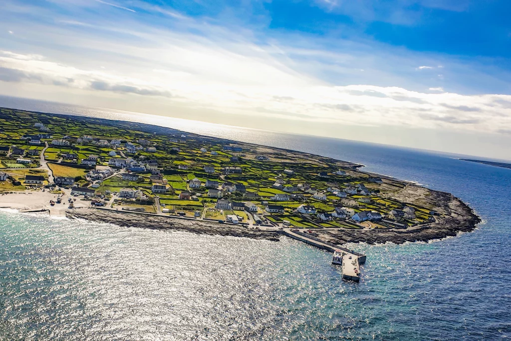 D1 - PSX_20190503_161650 Áine Seoighe Aerial view of Inis Oírr, showcasing a coastal landscape with houses and green fields, leading to the shoreline and pier.