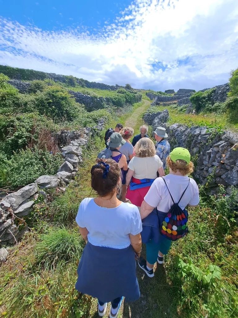 unnamed Group of retreat participants walking along a scenic path on Inis Oírr, surrounded by lush greenery and traditional stone walls, enjoying a wellness experience with Éalú Aran.